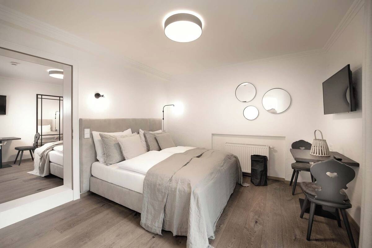 A modern bedroom with a bed, bedside tables, a desk, a chair, a mirror, and a radiator.