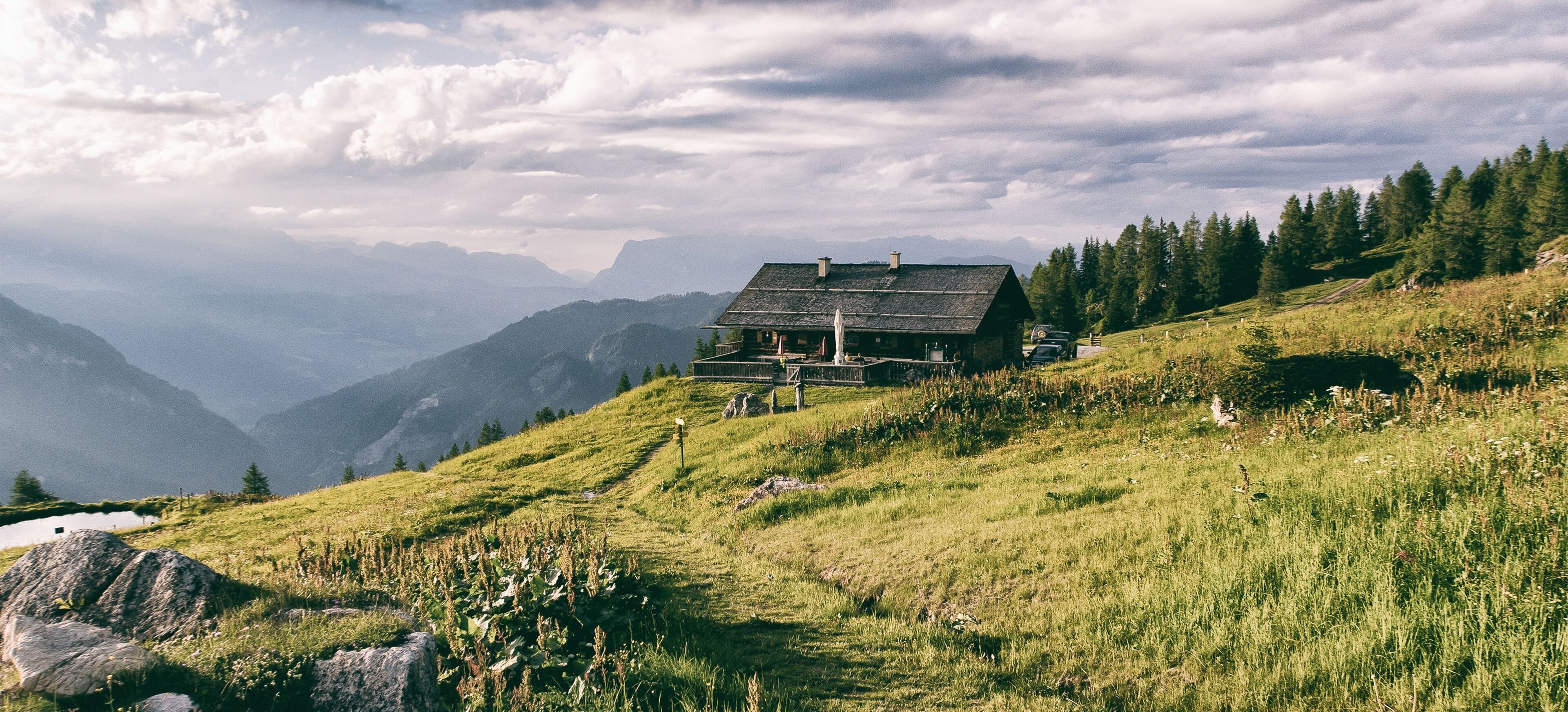 A mountain lodge with a stone exterior, a wooden deck, and a view of the surrounding mountains.
