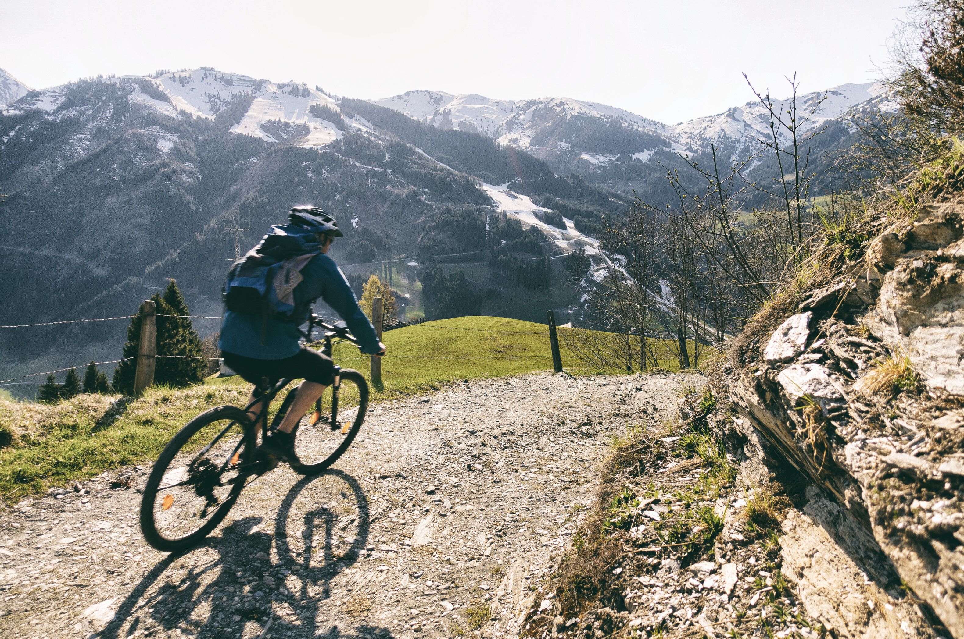 Ciclista de montaña en un sendero de tierra, con montañas nevadas al fondo.