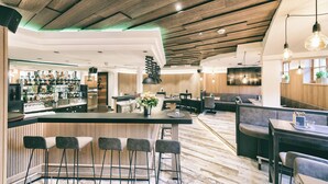 A modern bar area with a wooden ceiling, bar stools, and a counter with a variety of bottles and glasses. - Berg-Leben (Grossarl)