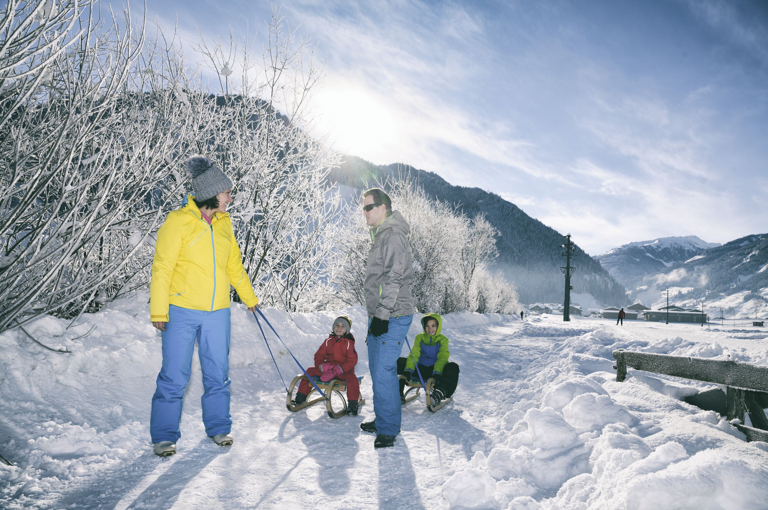 A snowy landscape with a person standing and two children on sleds.