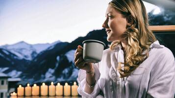 Una persona sosteniendo una taza, con velas y un paisaje montañoso de fondo.