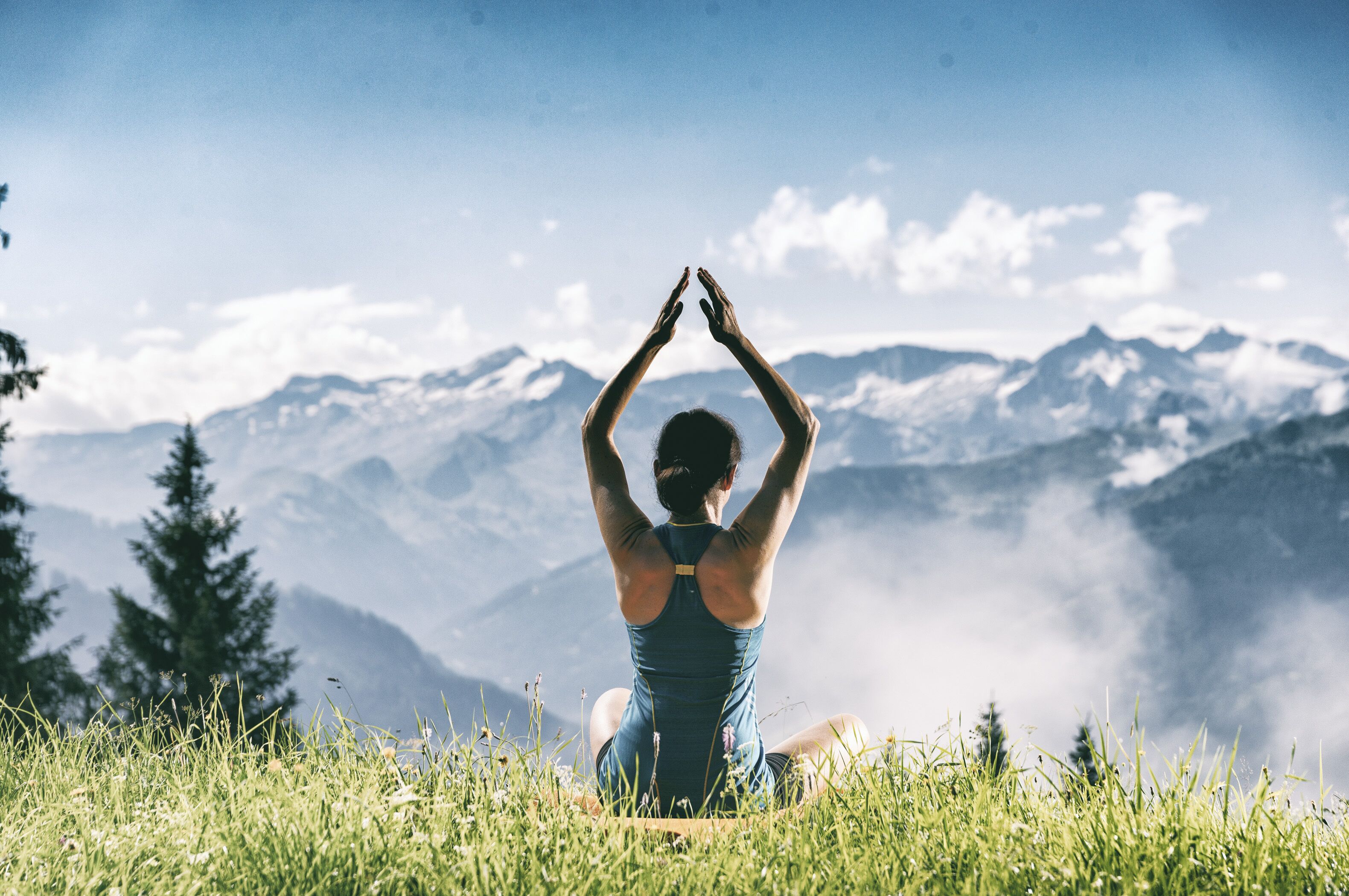 A person sitting on a grassy hill with a mountainous backdrop.