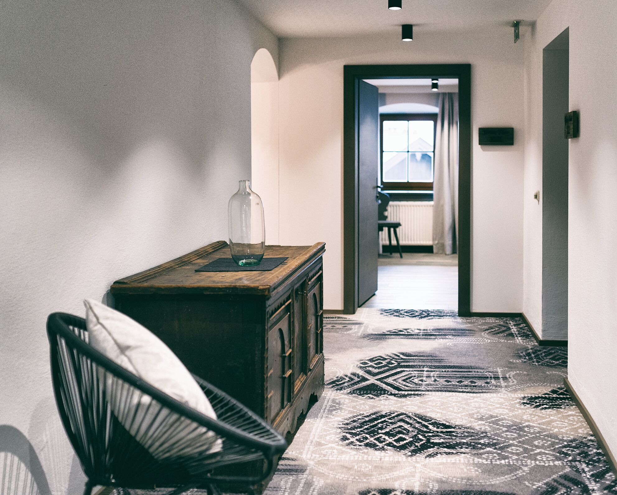 A narrow hallway with a patterned carpet, a wooden cabinet, and a chair.