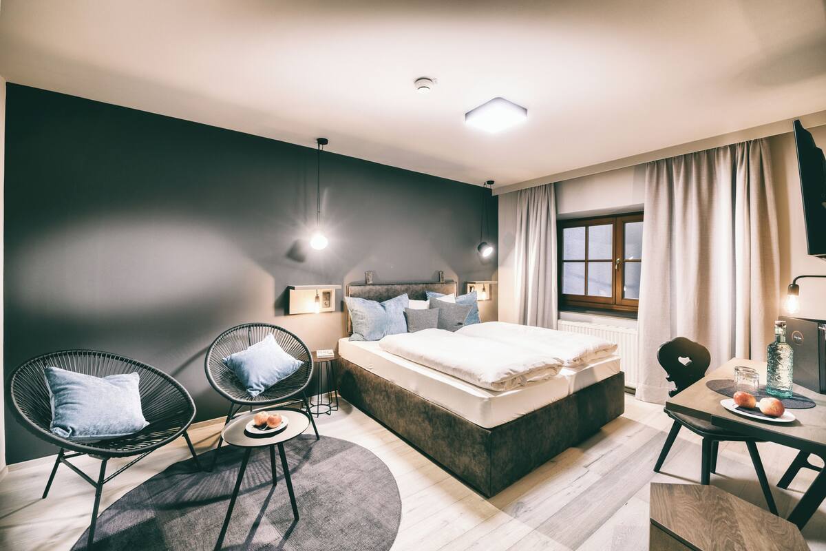 A modern bedroom with a bed, two chairs, a small table, and a window.