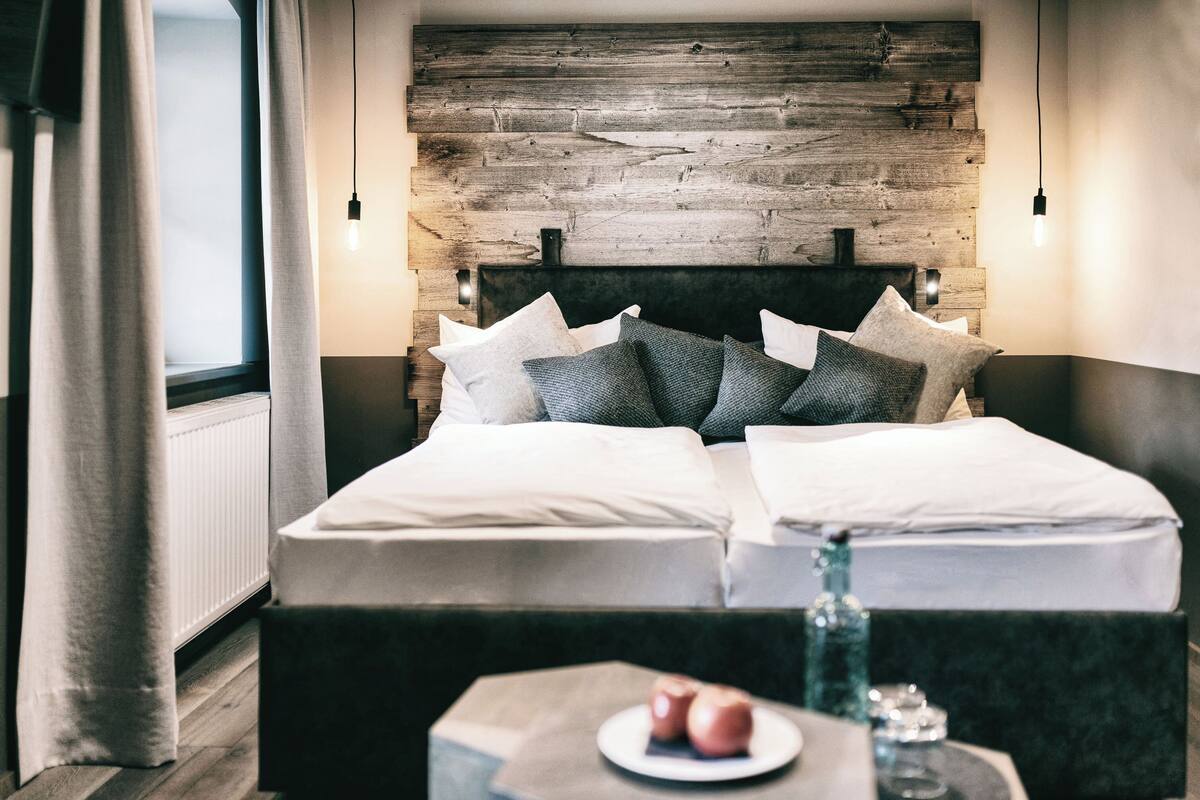 A modern bedroom with a wooden headboard, a bed with white linens, and a bedside table with a plate of apples and a glass.