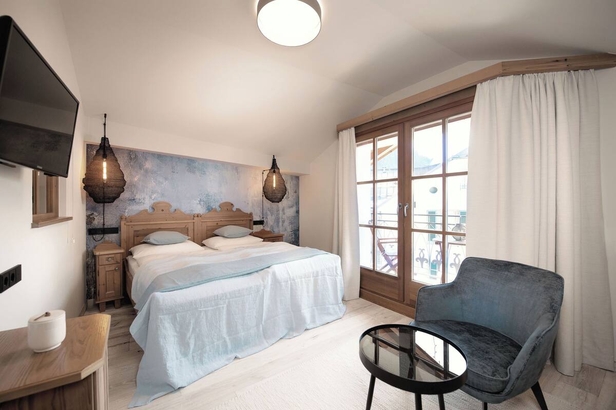 A bedroom with a bed, bedside tables, a TV, a chair, and a window with curtains.