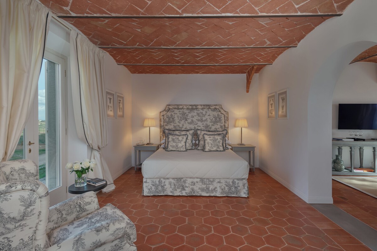Un dormitorio con una cama grande, dos mesitas de noche con lámparas, un televisor y vistas al exterior.