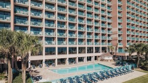 Un hotel con varios balcones, piscina y sillones de descanso.