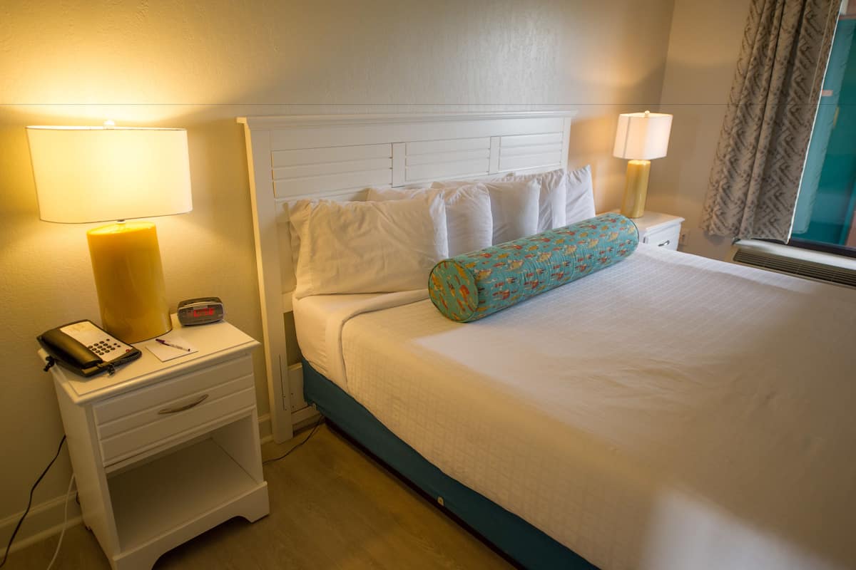 A hotel room with a bed, two bedside tables, a lamp, a clock, and a telephone on one of the tables.