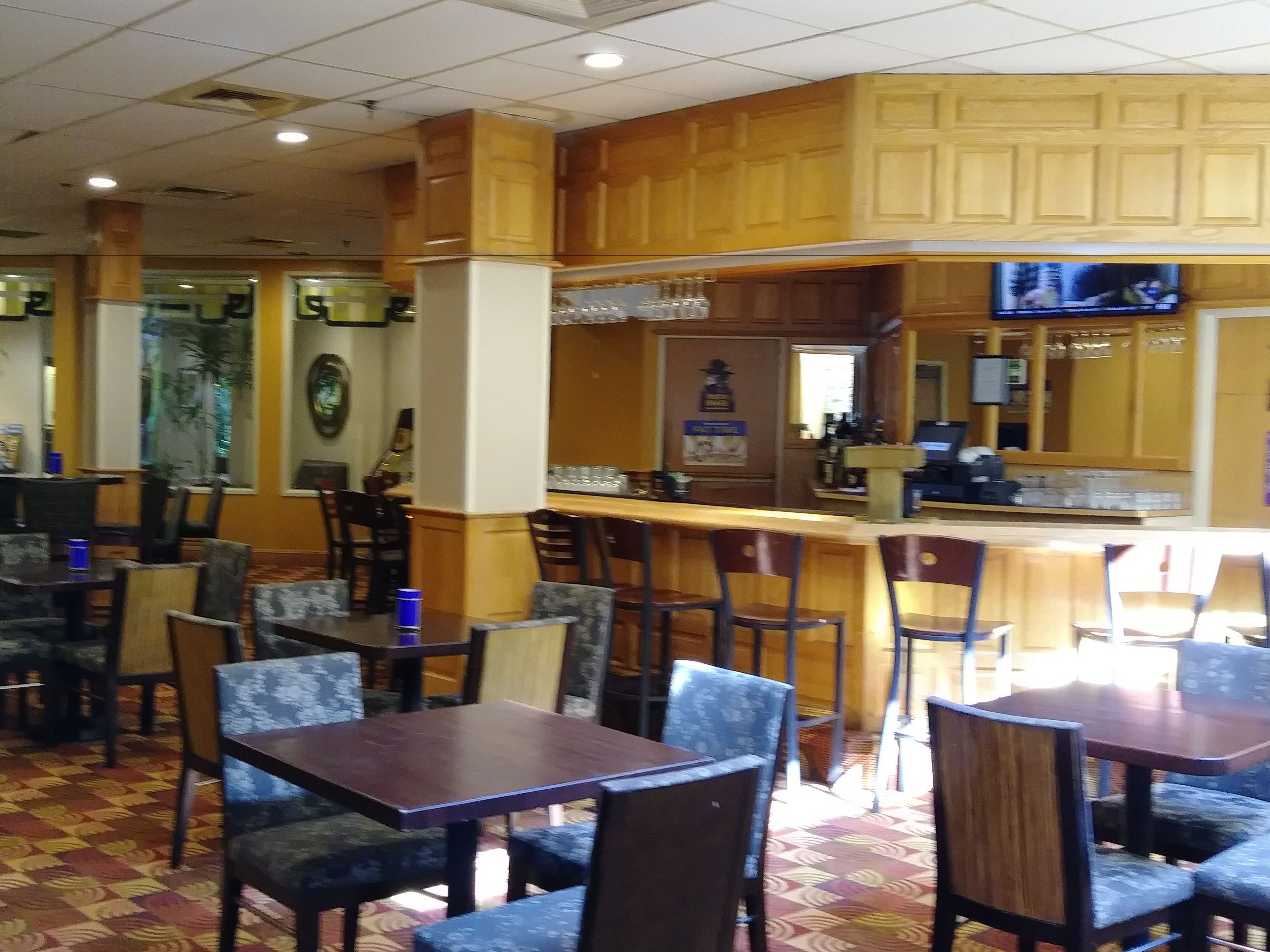 A restaurant with wooden paneling, a bar area, and multiple tables and chairs.