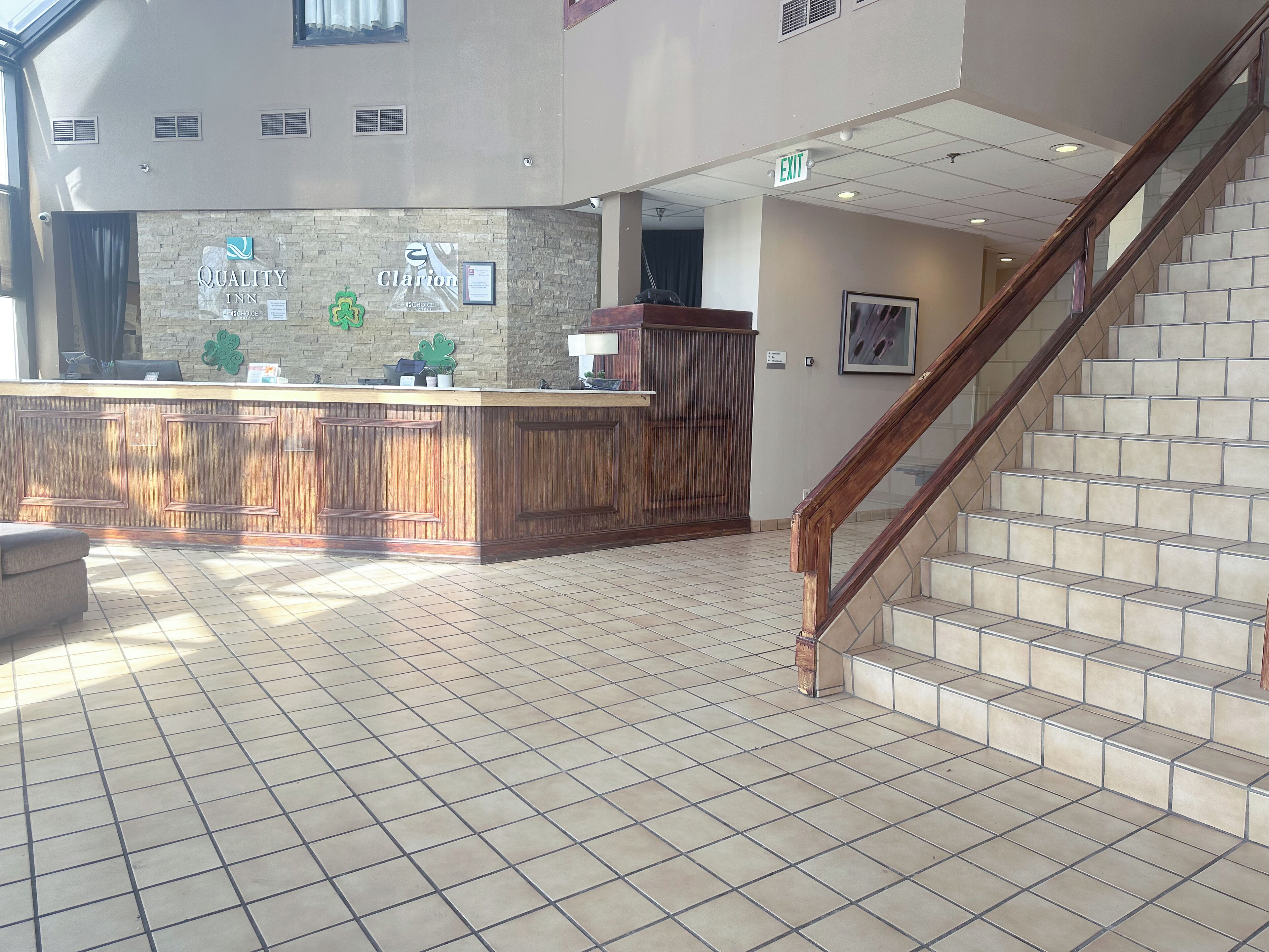 Ein Hotel-Empfangsbereich mit einer Rezeption, einer Treppe und Fliesenböden.