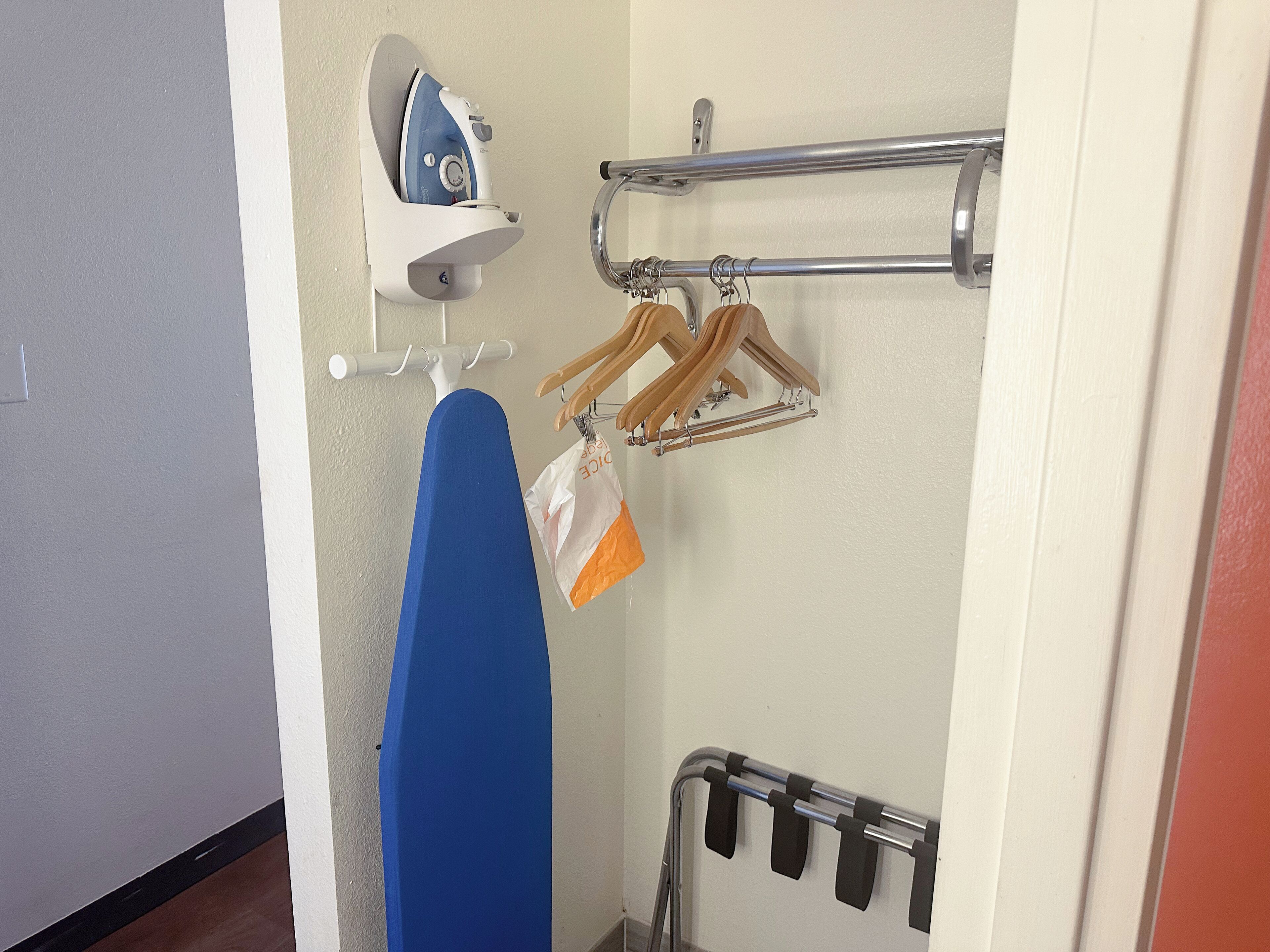 A bathroom with a blue towel hanging on a rack, a white iron, and wooden hangers on a metal rack.