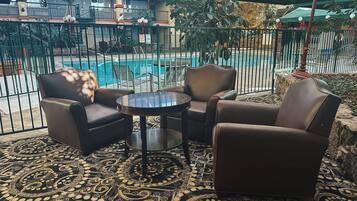 A balcony with a pool view, furnished with leather chairs and a small table, featuring a patterned carpet.