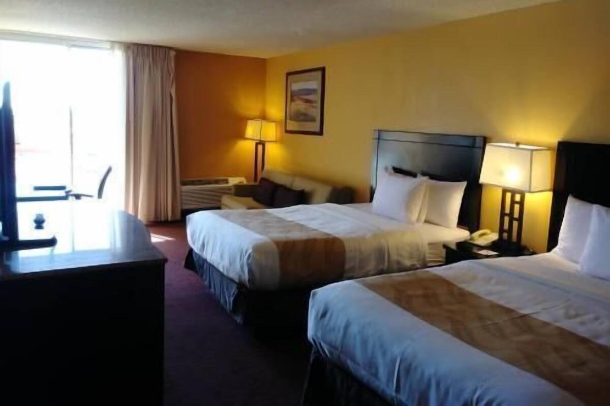 A hotel room with two beds, a desk, a chair, a lamp, and a window with curtains.