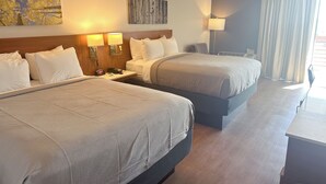 Une chambre d’hôtel avec deux lits, un bureau, une lampe et des œuvres d’art accrochées aux murs.