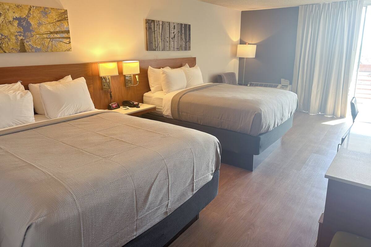 A hotel room with two beds, a desk, a lamp, and artwork on the walls.