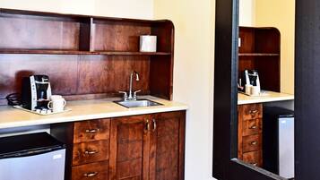 A compact kitchenette with a coffee maker, sink, and storage cabinets.