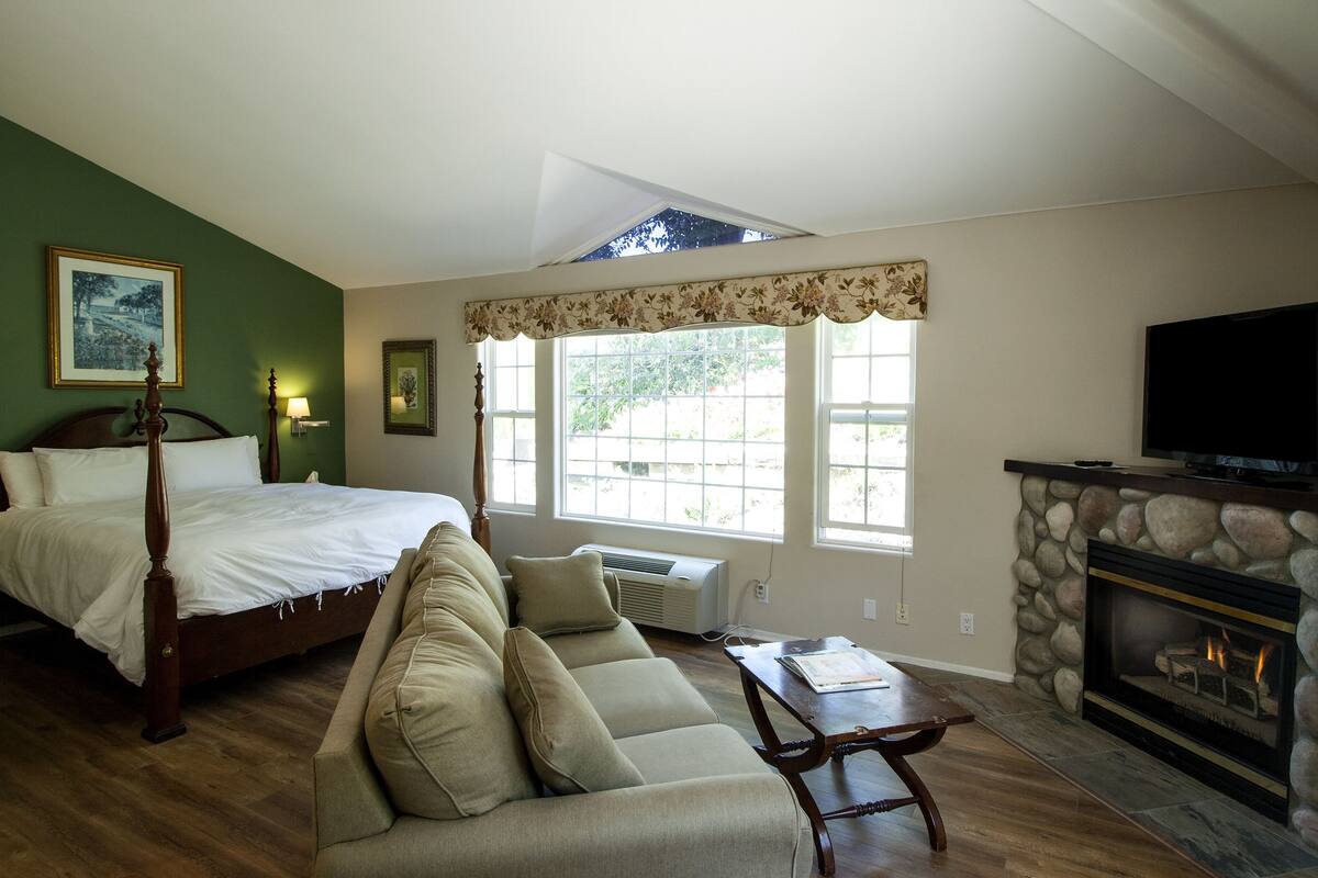 A bedroom with a four-poster bed, a sofa, a fireplace, and large windows.