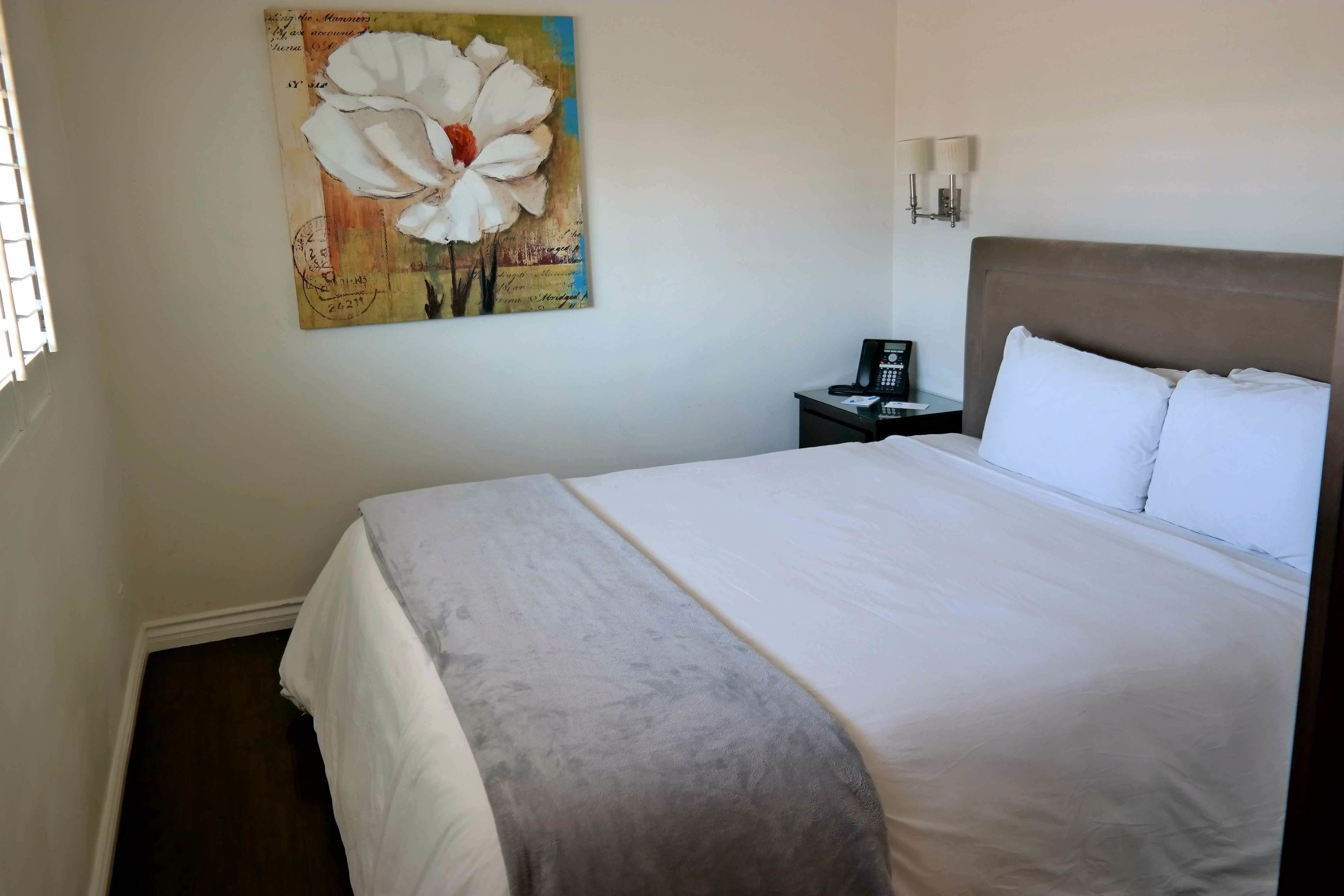Habitación de hotel con una cama grande, una mesita de noche, un teléfono y una lámpara de pared.