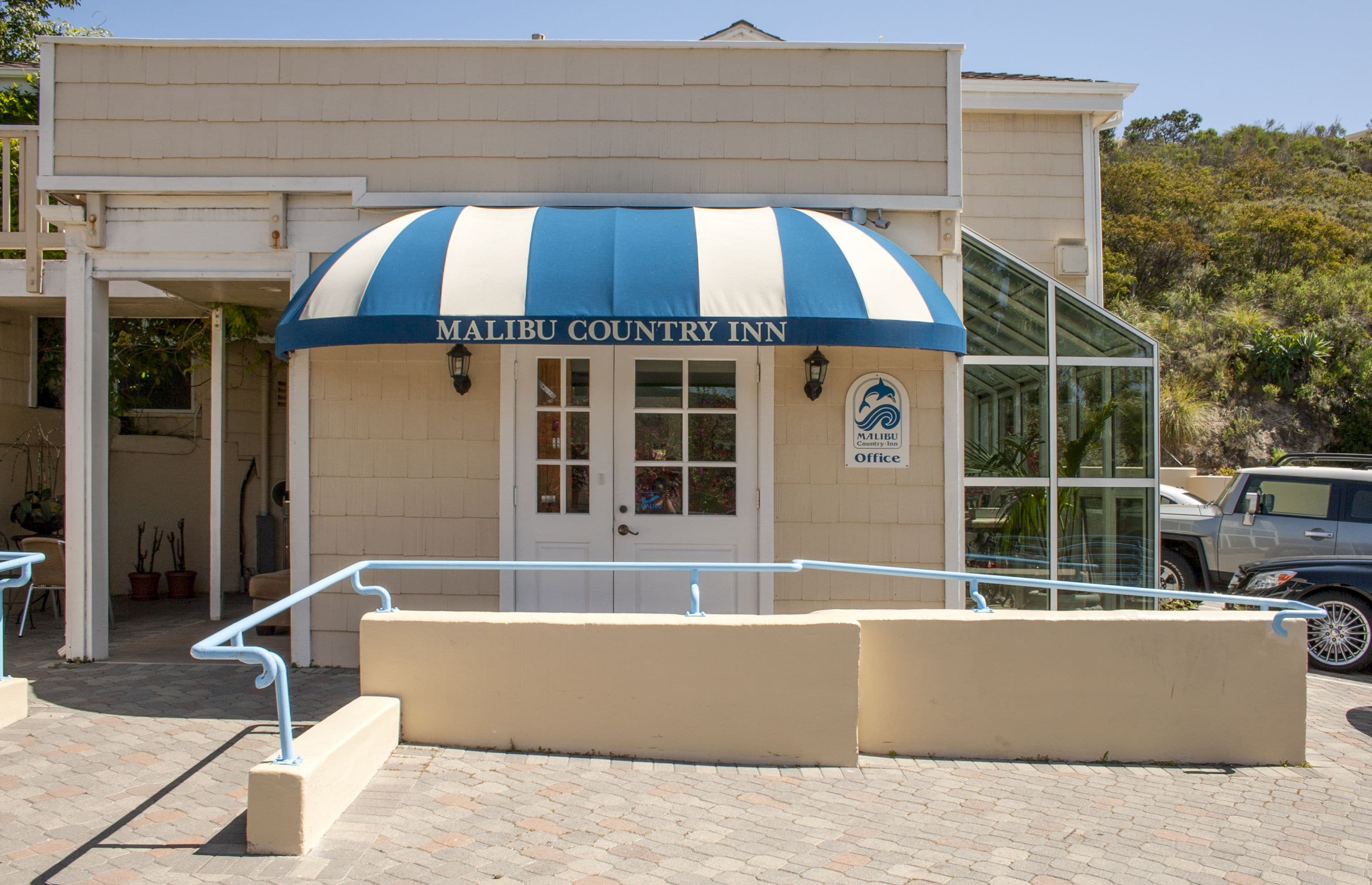El Malibu Country Inn, con un toldo azul y blanco a rayas, una puerta de cristal de entrada y un estacionamiento visible al fondo.