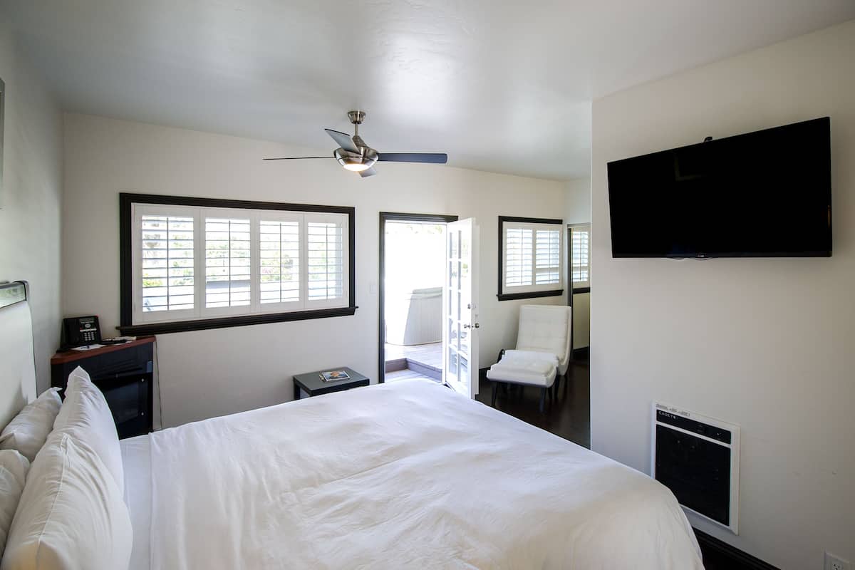 A hotel room with a bed, a desk, a chair, a television, and a ceiling fan.