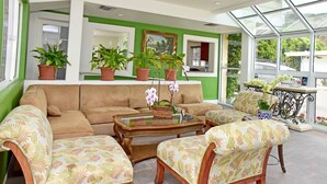 A sunlit room with a beige sofa, floral-patterned chairs, and a glass coffee table.