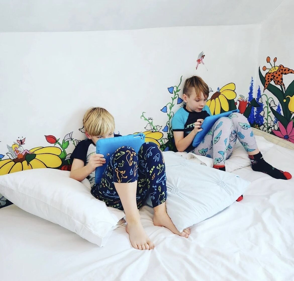Dos niños acostados en una cama con un mural de pared colorido.