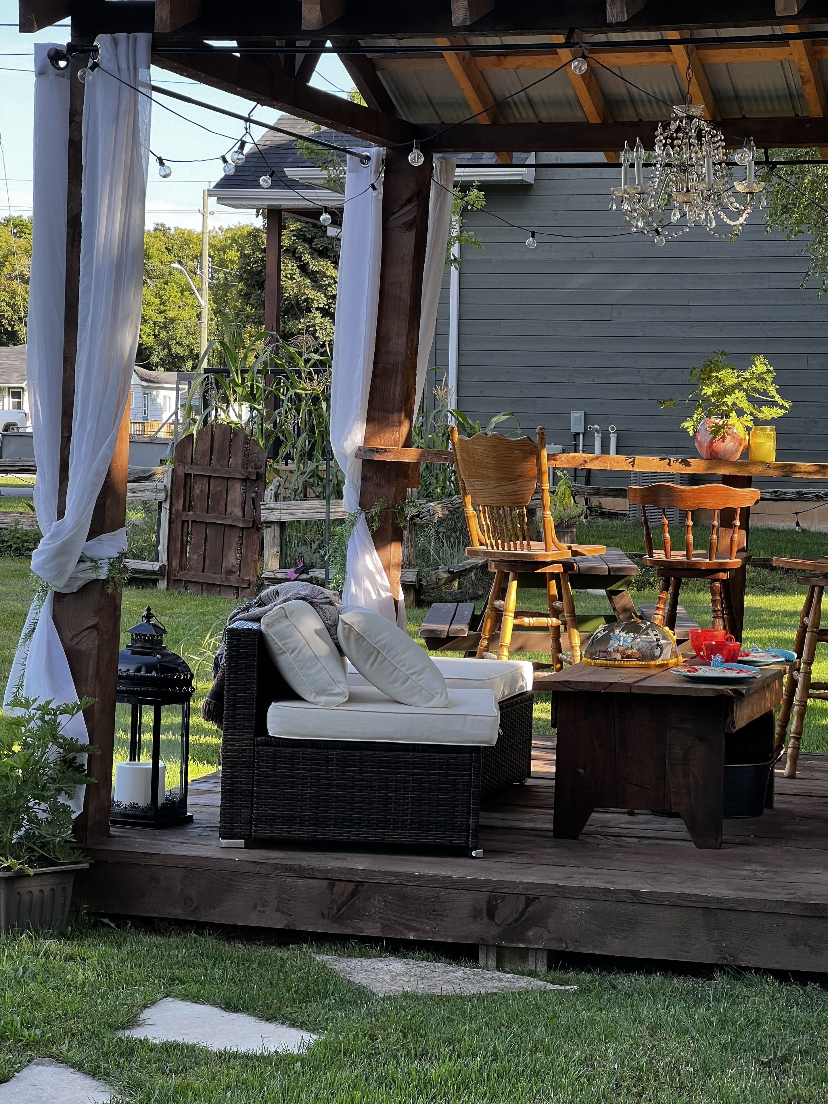 An outdoor patio with wicker furniture, a wooden table, and a chandelier.