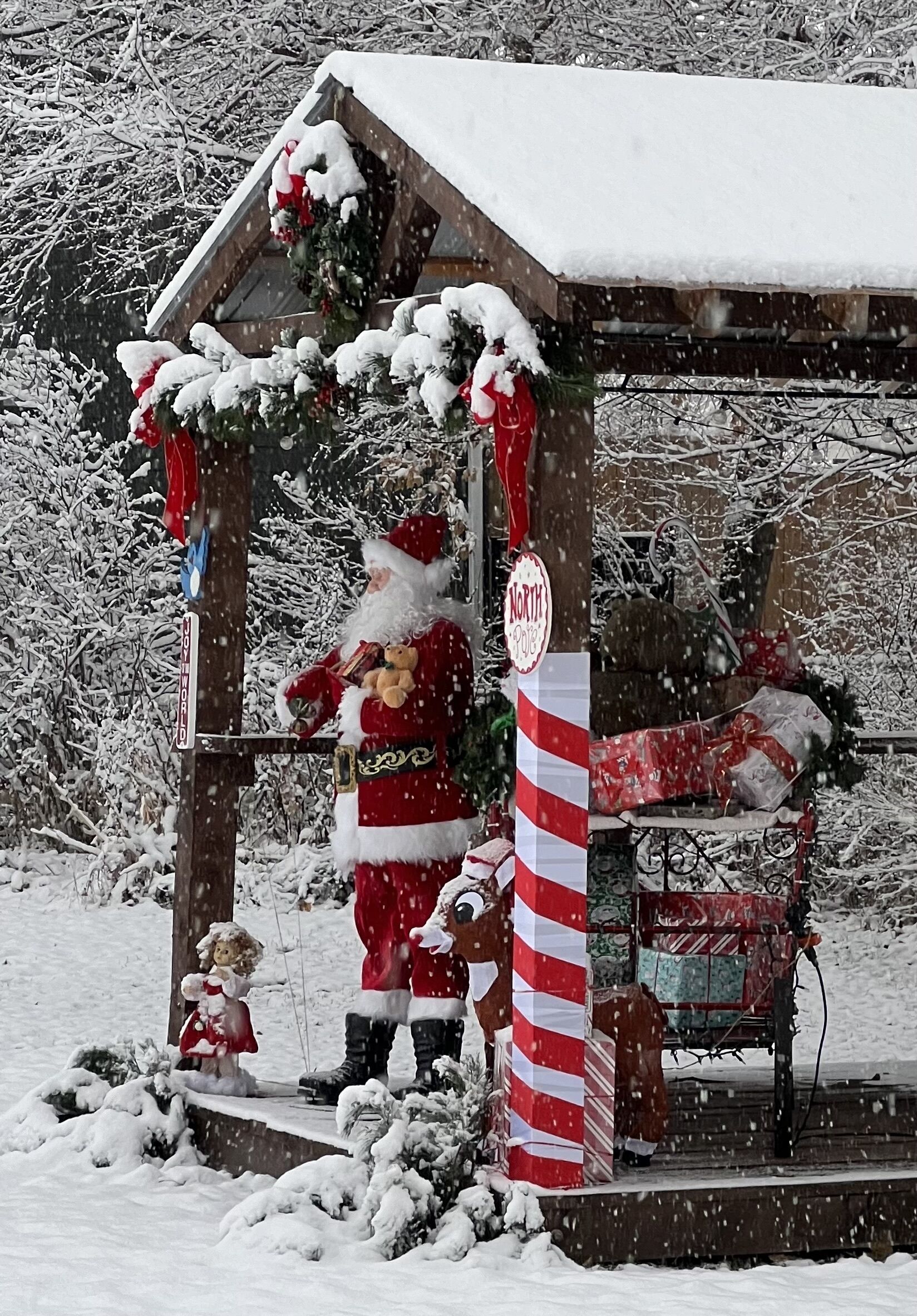 Un espacio exterior cubierto de nieve con una estructura de madera, un letrero que dice 'North Pole' y una decoración con forma de bastón de caramelo.