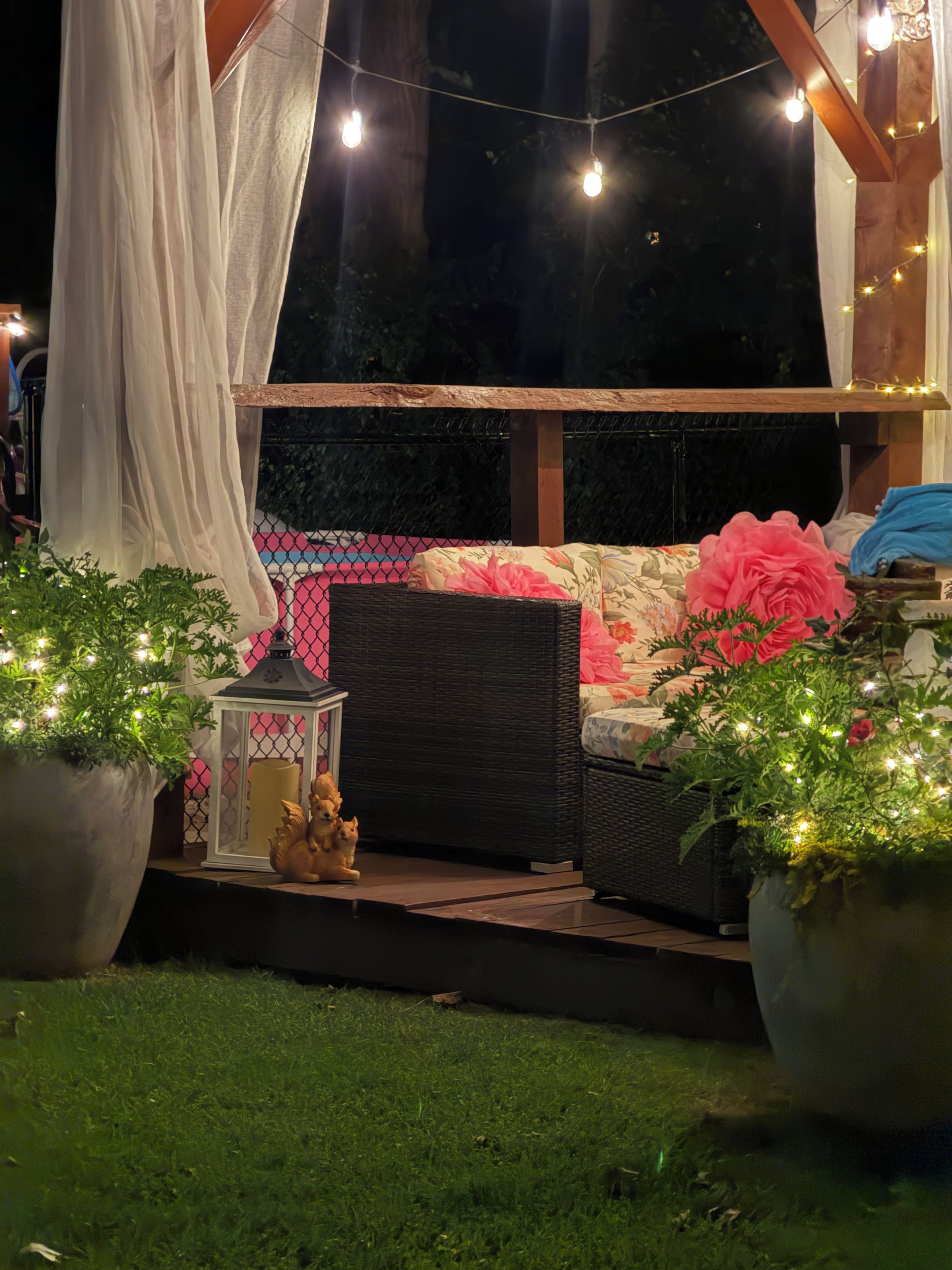 Un espace extérieur aménagé avec des guirlandes lumineuses, un canapé en osier et des plantes en pot.
