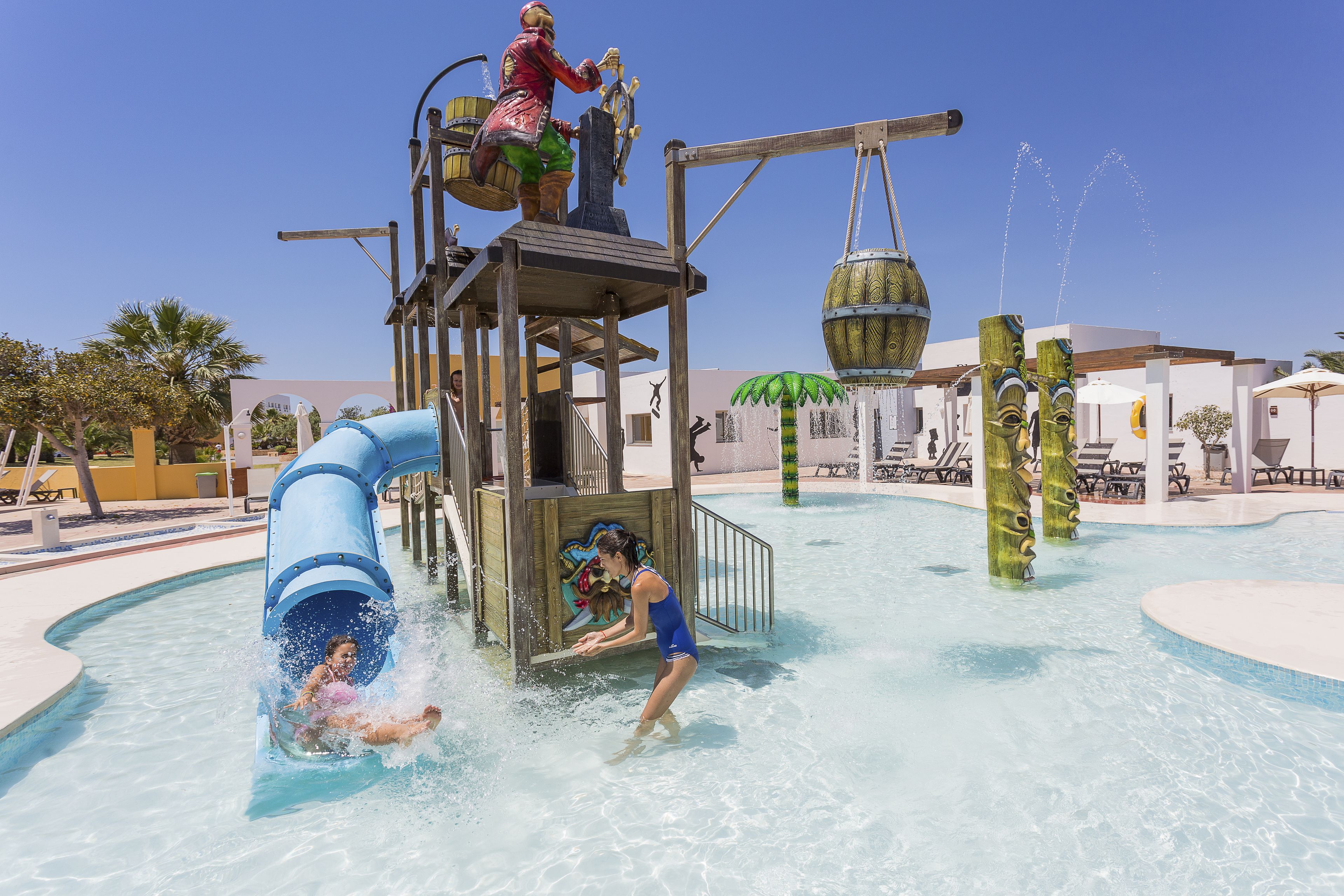 A water park with a blue slide, a water play structure, and a pool area.