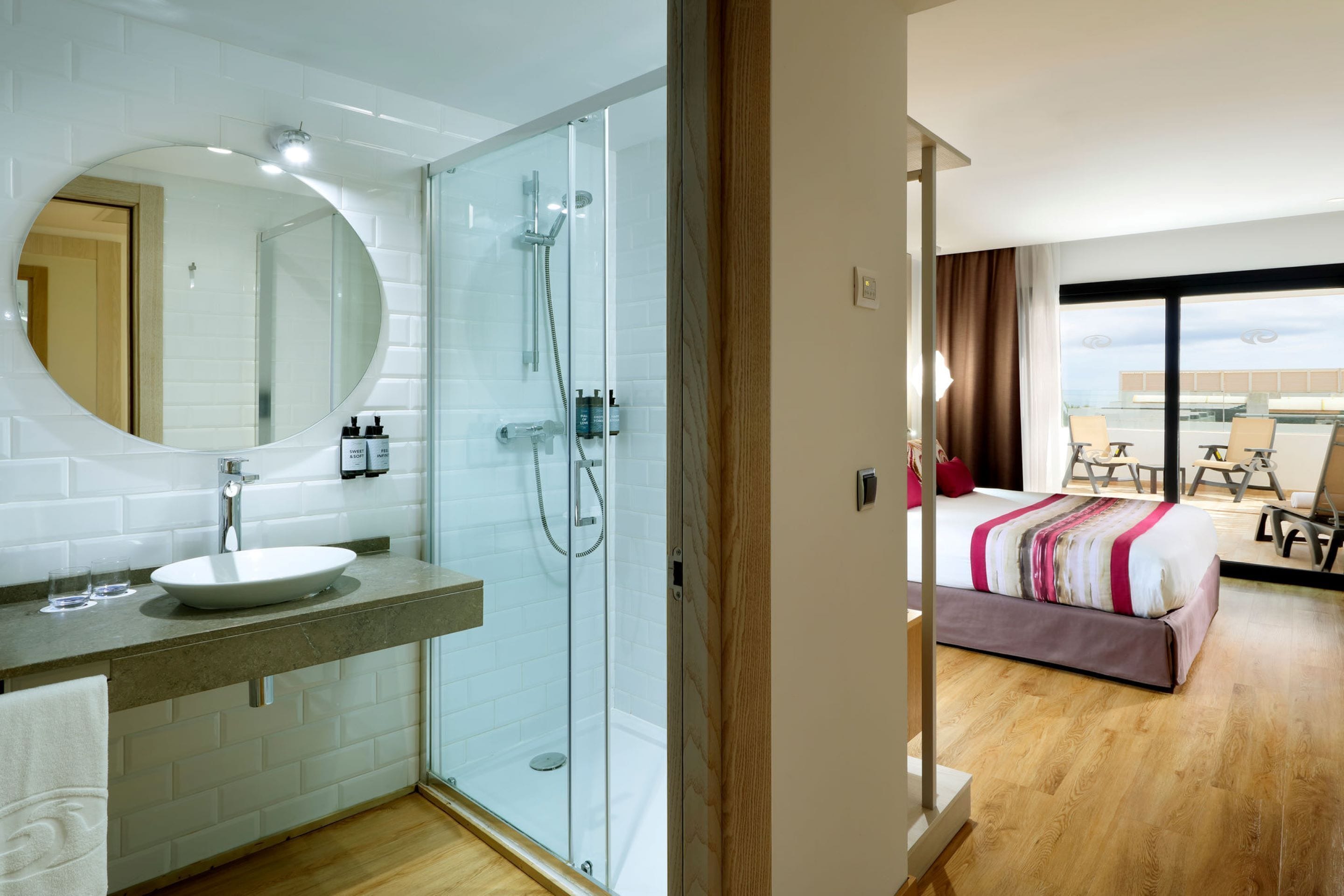 Une salle de bain moderne avec une douche à parois de verre, un miroir rond et un lavabo blanc.