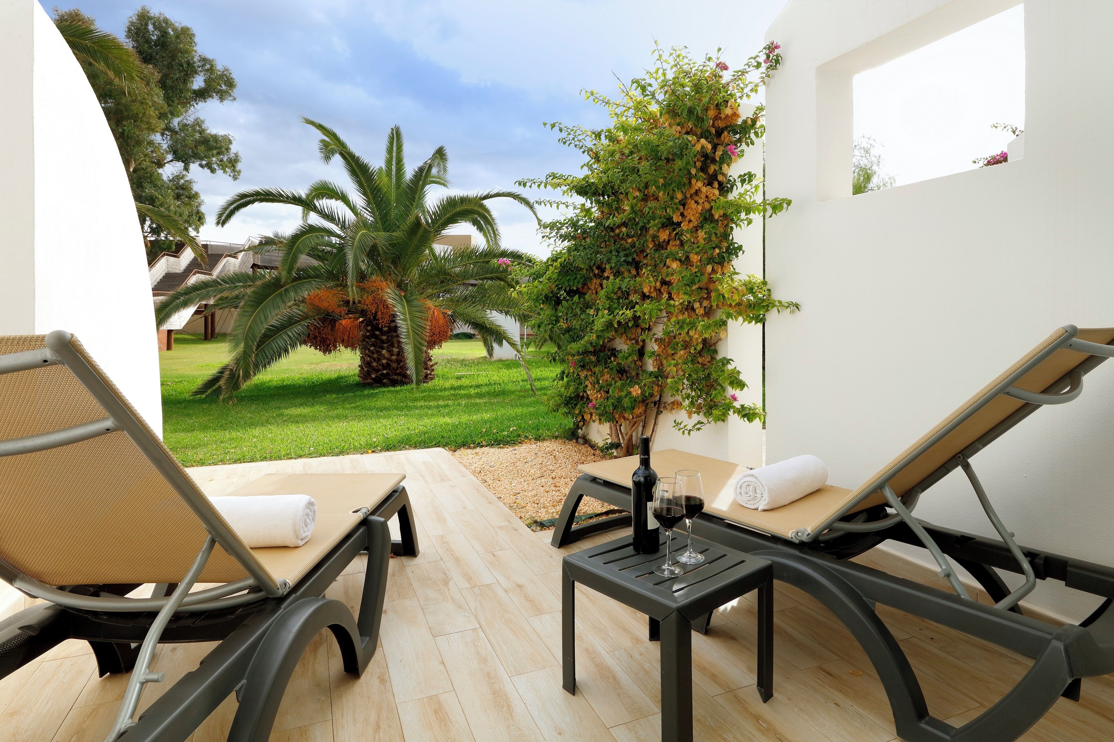 A sunlit outdoor seating area with two lounge chairs, a small table, and a bottle of wine.