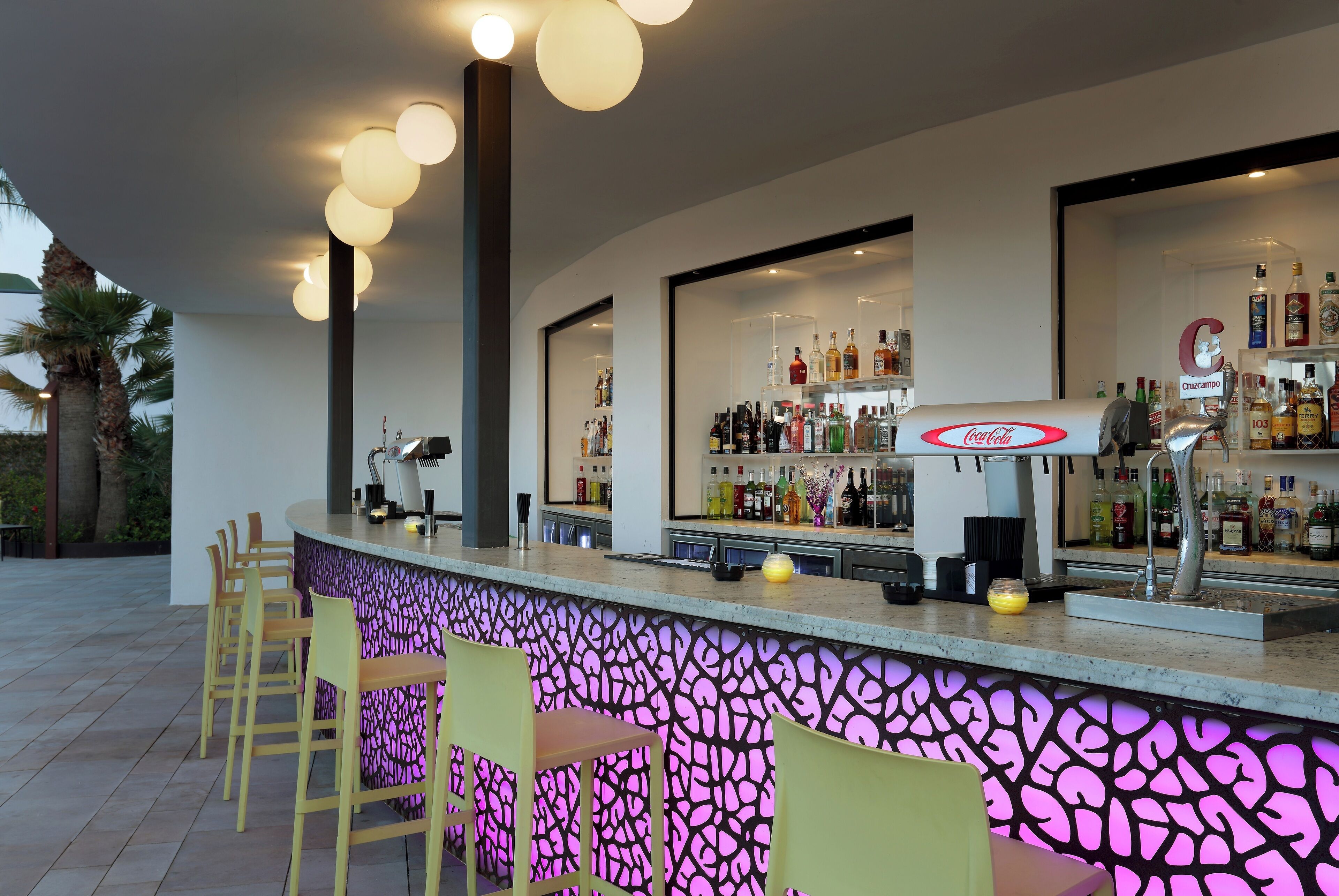 Eine Bar mit einer Theke, Barhocker und Regalen voller Flaschen verschiedener Sorten.