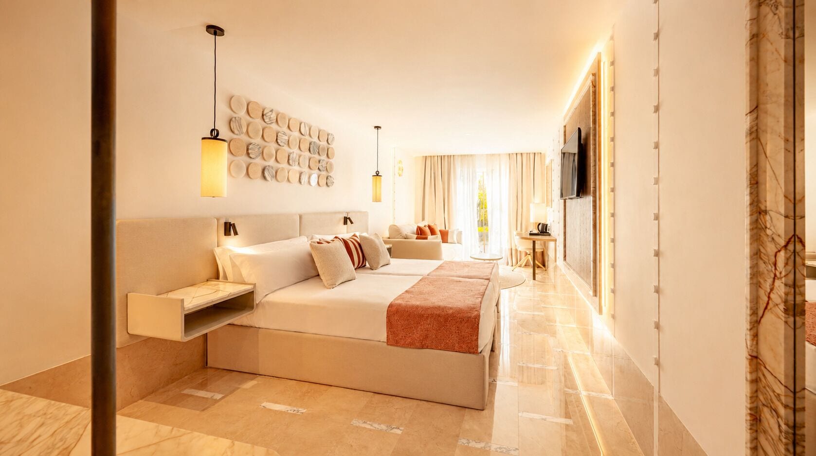 A modern hotel room with a large bed, bedside tables, a TV, and a wall-mounted light fixture.
