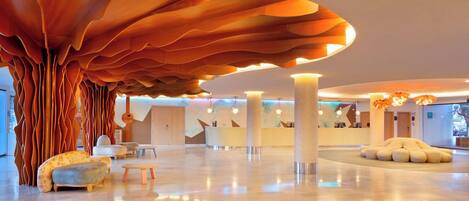 A spacious lobby with a unique ceiling design, a reception desk, and comfortable seating areas.