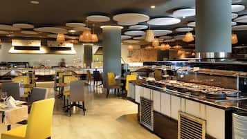 Ein modernes Restaurant mit einem zentralen Buffet, gelben und grauen Stühlen und Pendelleuchten.