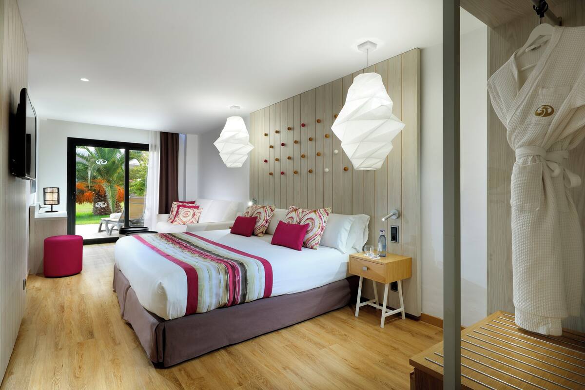 Habitación de hotel moderna con una cama grande, suelo de madera, televisión y vistas al exterior.