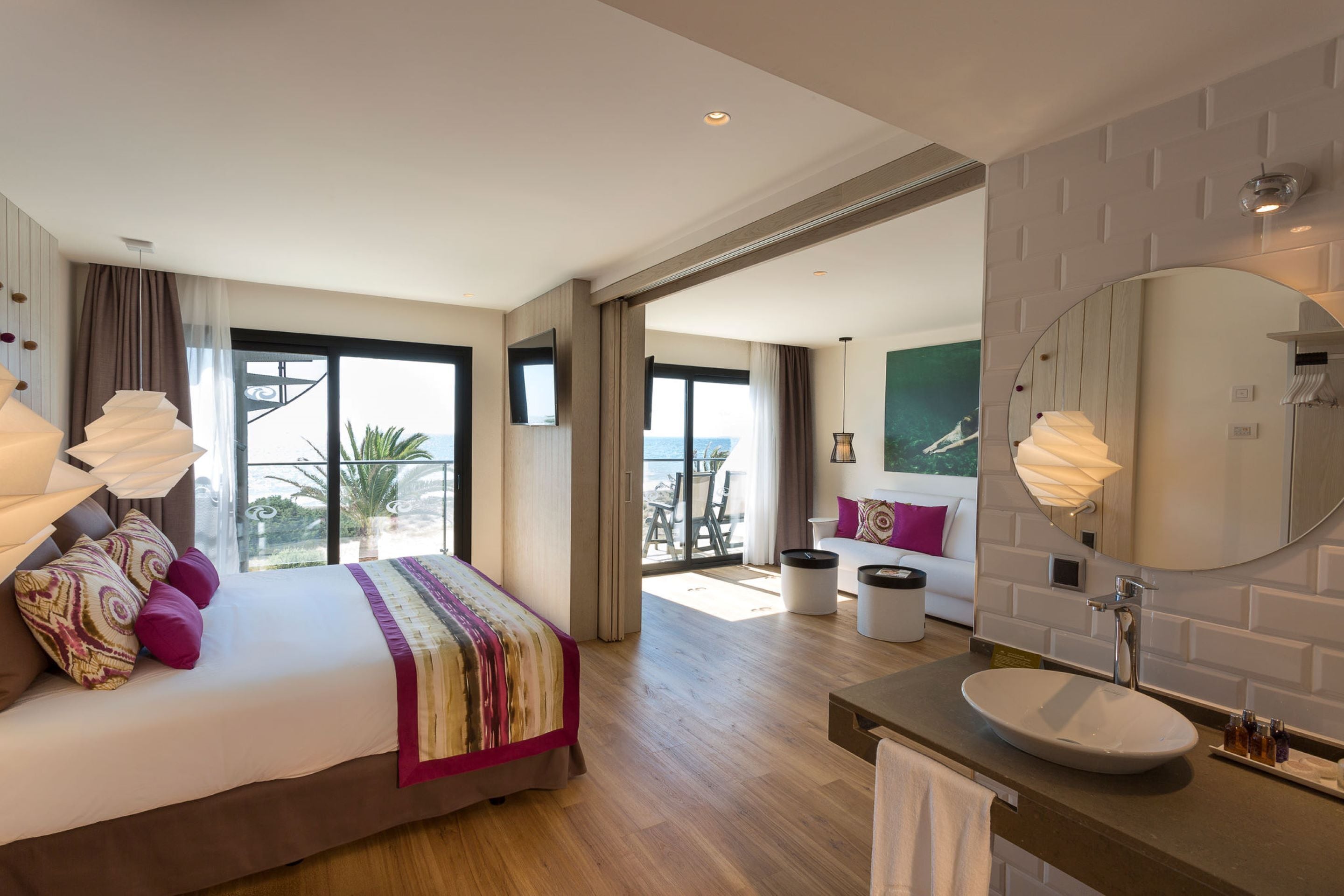 Una habitación de hotel moderna con una cama grande, un baño con espejo redondo y un balcón con vistas.