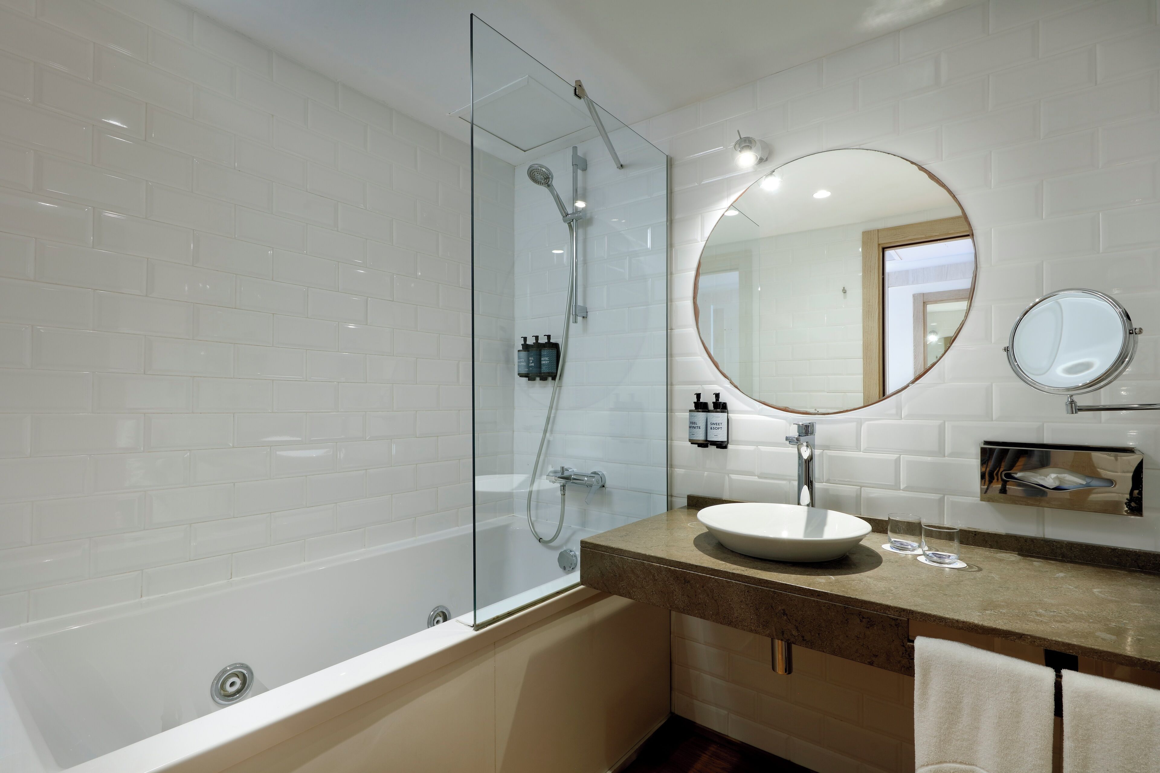 A modern bathroom with a glass-enclosed shower, a round mirror, and a sink with a marble countertop.