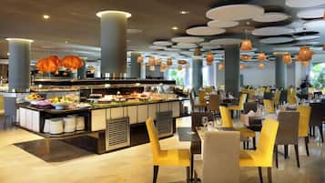 Un restaurante con zona de bufé, sillas amarillas y grises, y un diseño de techo moderno.