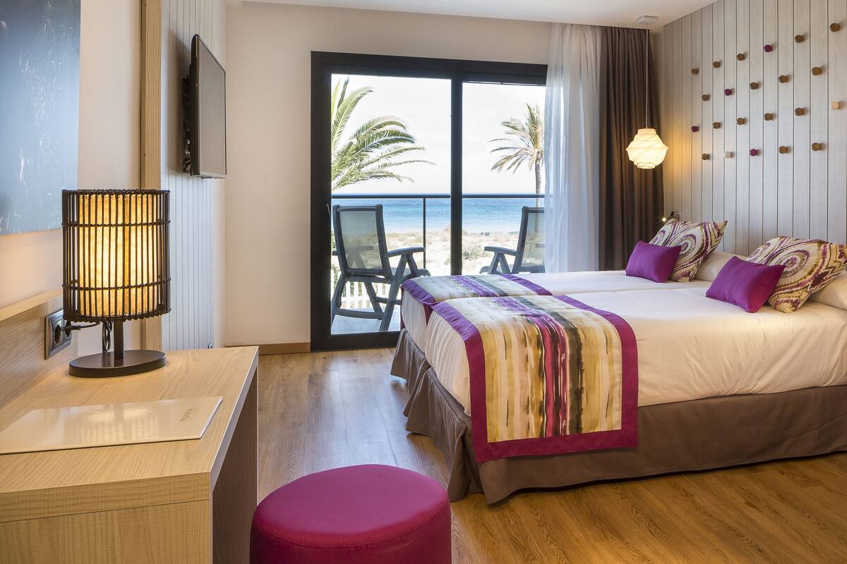 Habitación de hotel con cama, escritorio, silla y vista a la playa.