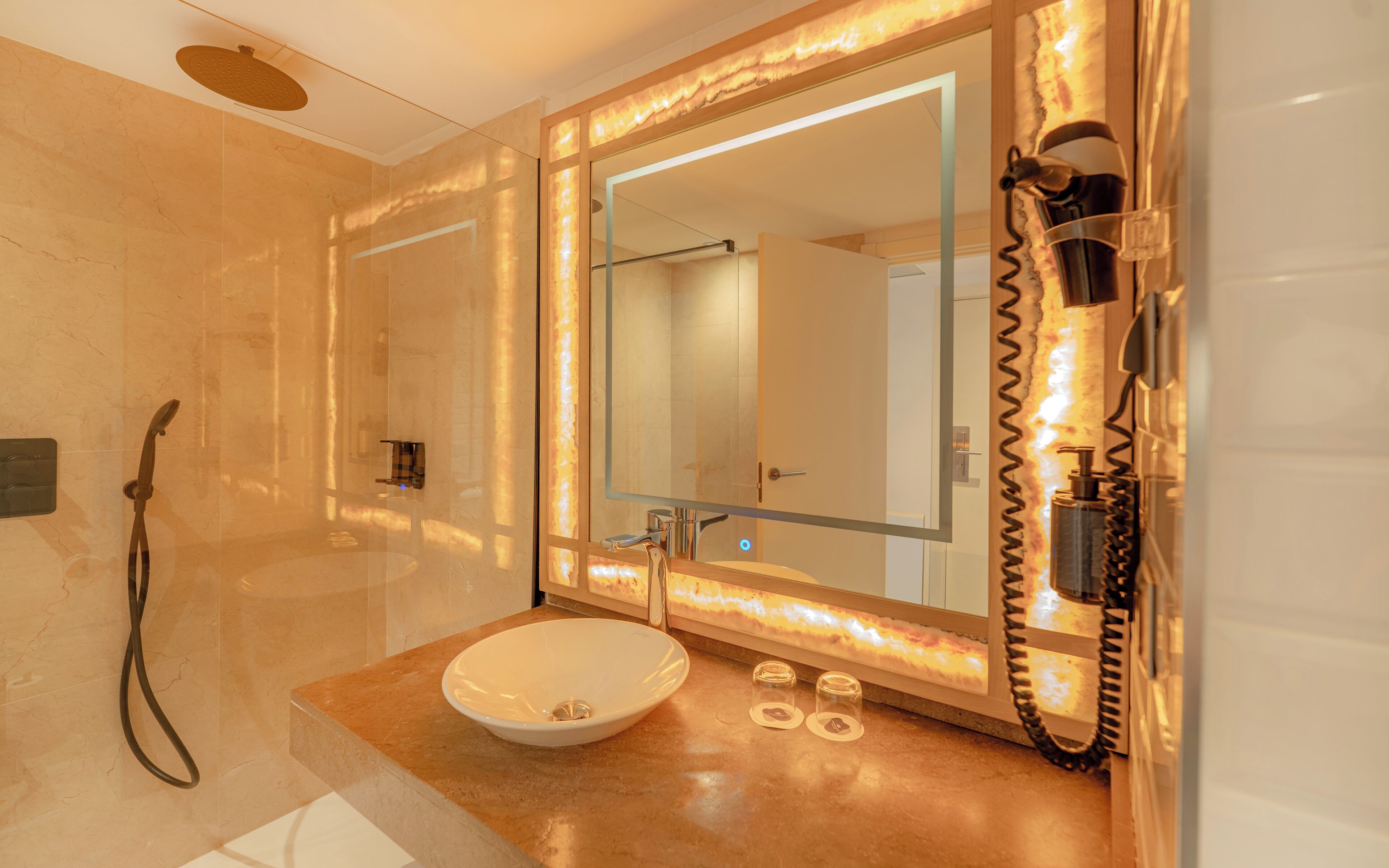 Un baño con un espejo grande, lavamanos, ducha y secador de pelo.