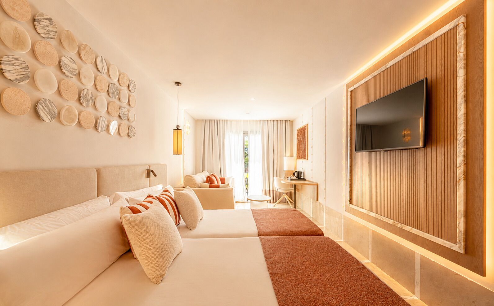 Una habitación de hotel moderna con una cama grande, un sofá, un televisor montado en la pared y un diseño decorativo en la pared con patrones circulares.
