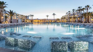 A swimming pool with mosaic tiles, surrounded by palm trees and hotel buildings. - Grand Palladium White Island Resort & Spa - All Inclusive (Sant Josep de sa Talaia)