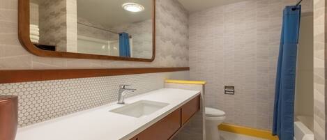 A bathroom with a white sink, mirror, and toilet, with patterned tiles and a blue shower curtain.