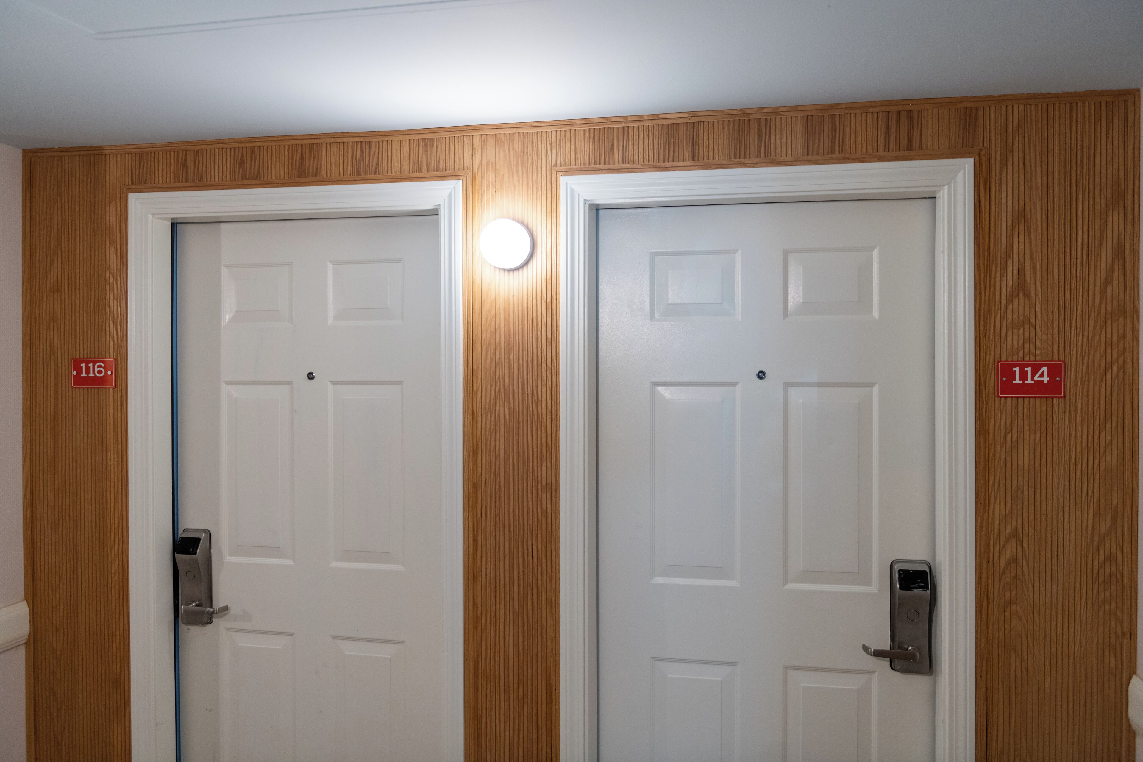 Two white doors with numbers 116 and 114, wooden paneling, and a light fixture above the doors.