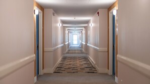 A long, narrow hotel hallway with a patterned carpet, white walls, and doors on both sides. - Driftaway Hotel and Pool (Ogunquit)