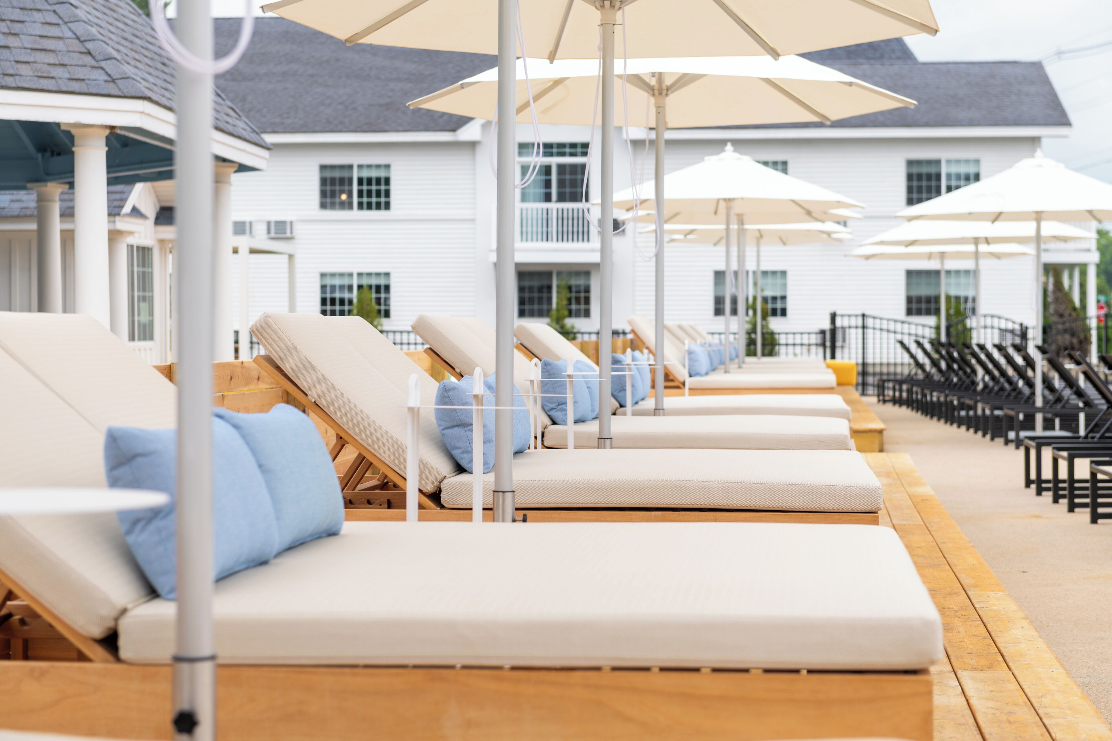 A row of sun loungers with umbrellas, wooden deck, and a white building in the background.